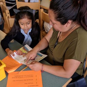 Child sitting with a family member that is pointing out a word in a children's book at a Springboard Collaborative family workshop