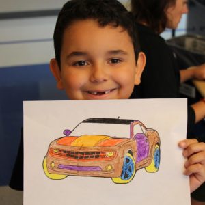 Child holding up a colored-in race car coloring book picture and smiling