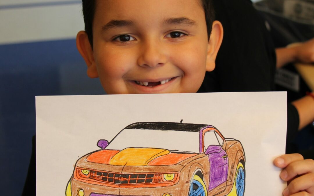 Child holding up a colored-in race car coloring book picture and smiling