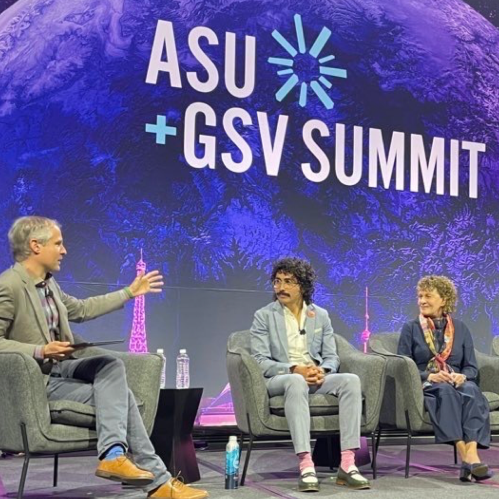 Three people sitting on a stage engaged in a discussion with the ASU + GSV Summit logo in the background.